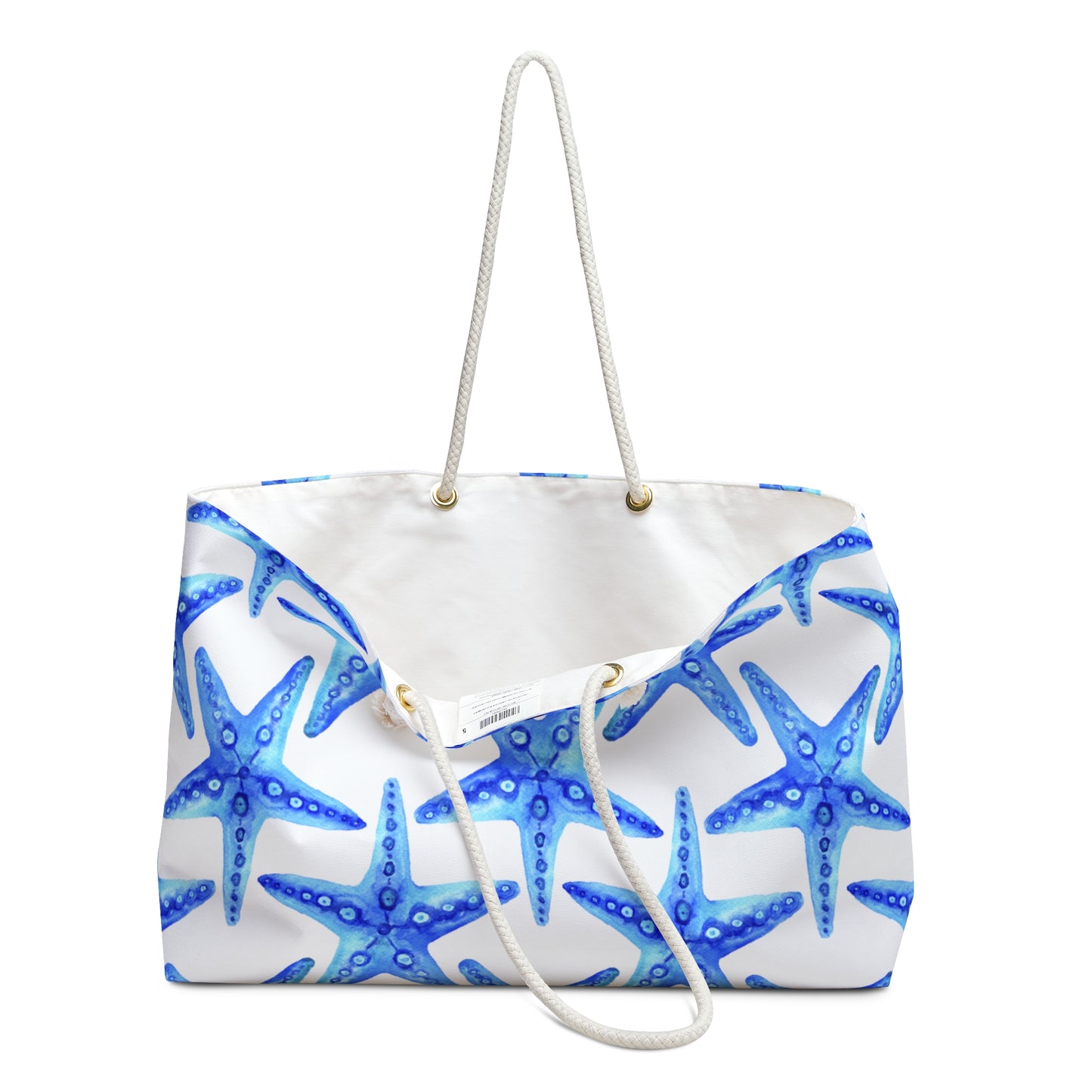 Oversized beach tote with bold blue starfish pattern on white background with rope handles. Bag is opened to show the white-liner inside.