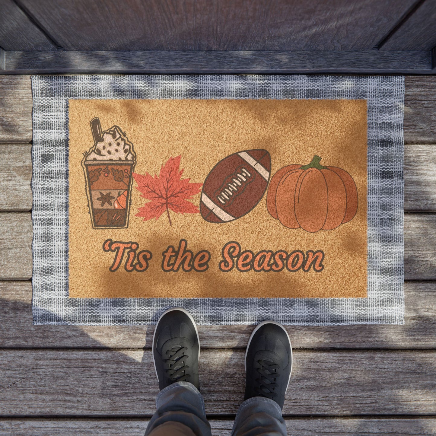 Doormat with autumn-themed design featuring a coffee cup, leaf, football, and pumpkin on a wooden floor.