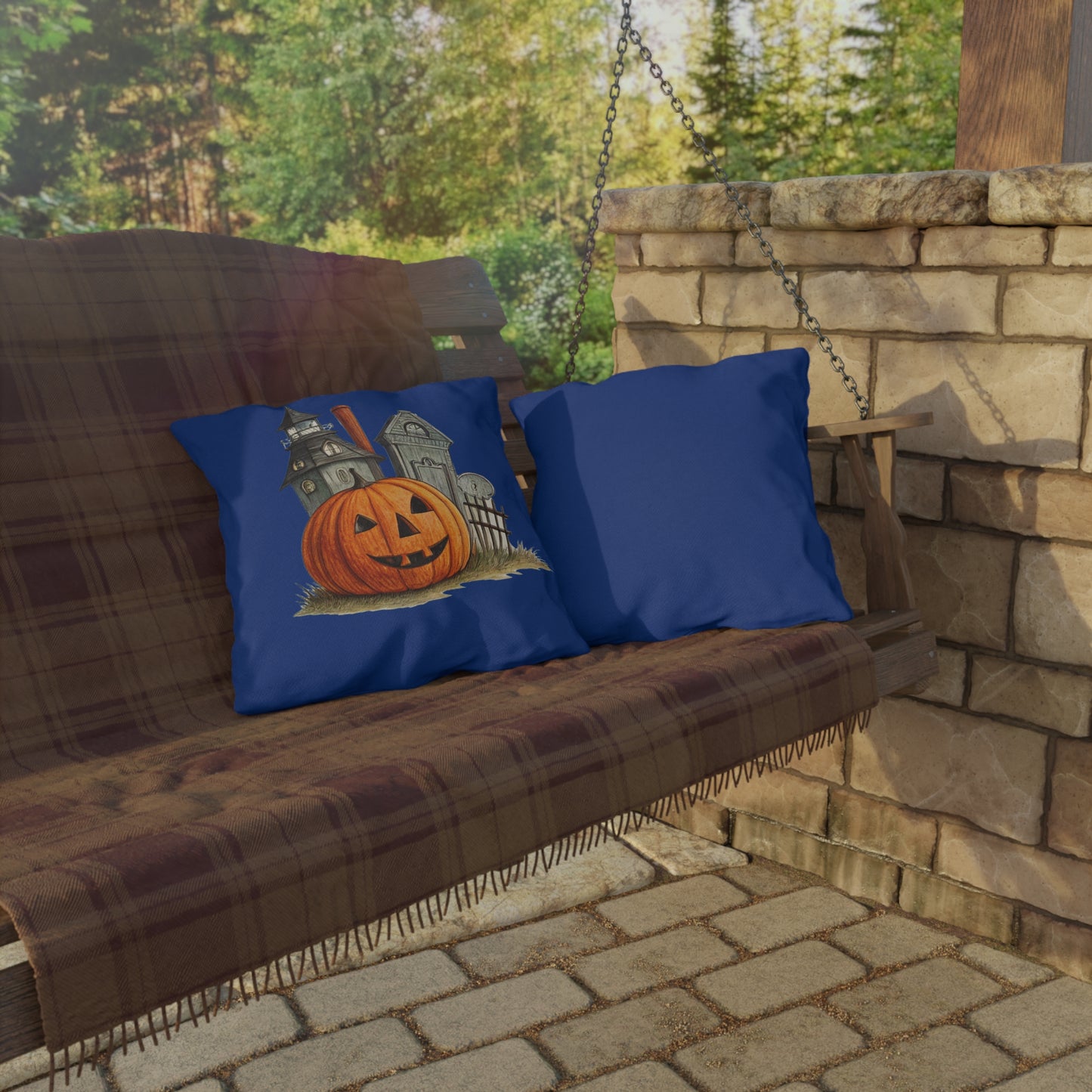 Wooden porch swing with blue pillows featuring Halloween designs, set against a stone wall and greenery.