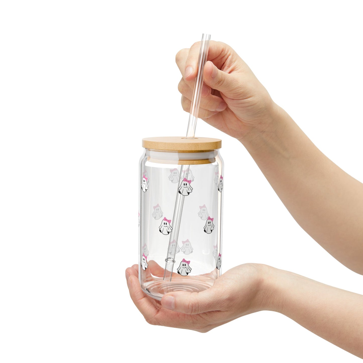Clear glass tumbler with bamboo lid and straw held by a hand on a white background