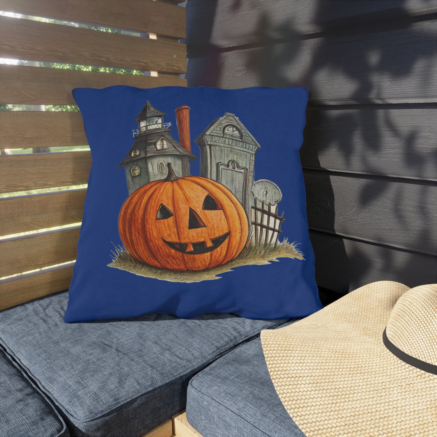 Decorative pillow with Halloween design featuring a pumpkin and haunted house on a blue background, placed on a wooden bench.