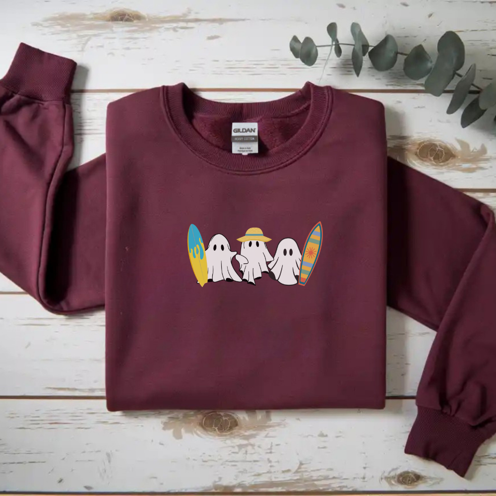 Maroon sweatshirt with ghost and surfboard design on a wooden surface