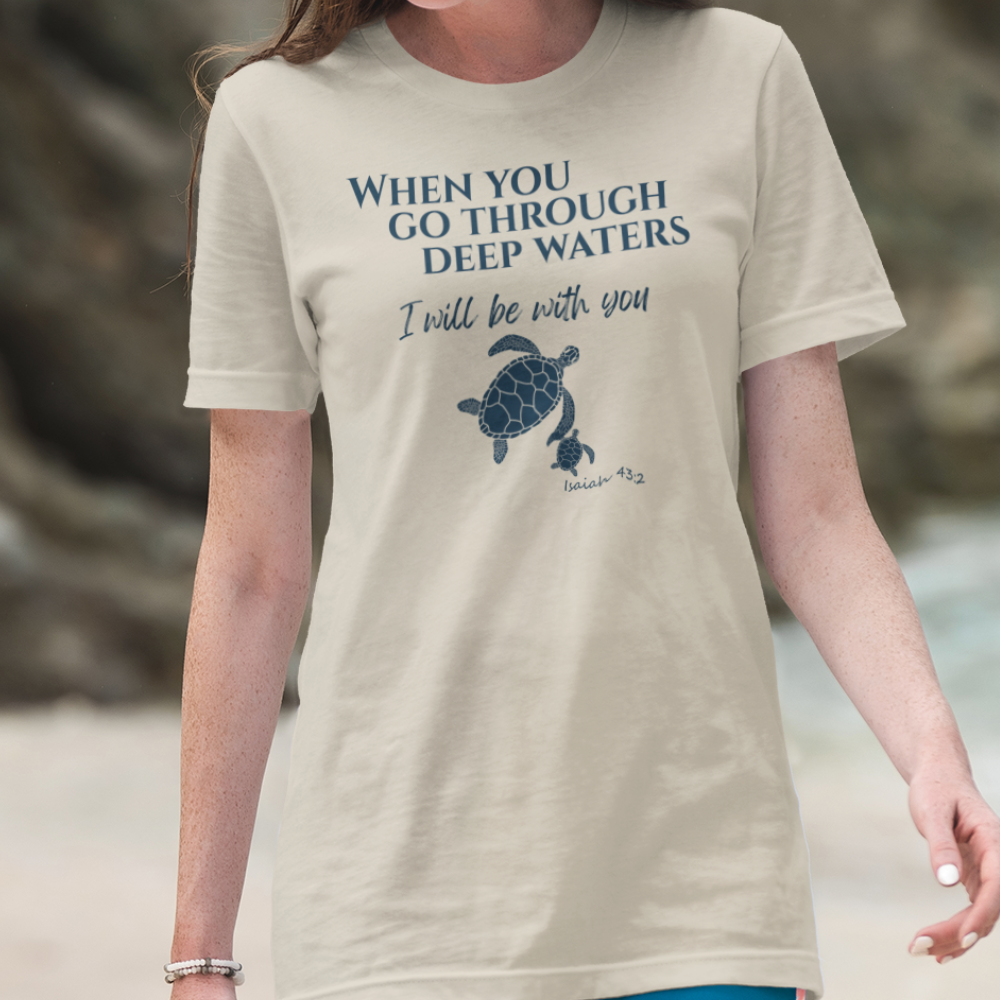 Person wearing a t-shirt with a turtle graphic and motivational quote on a beach.
