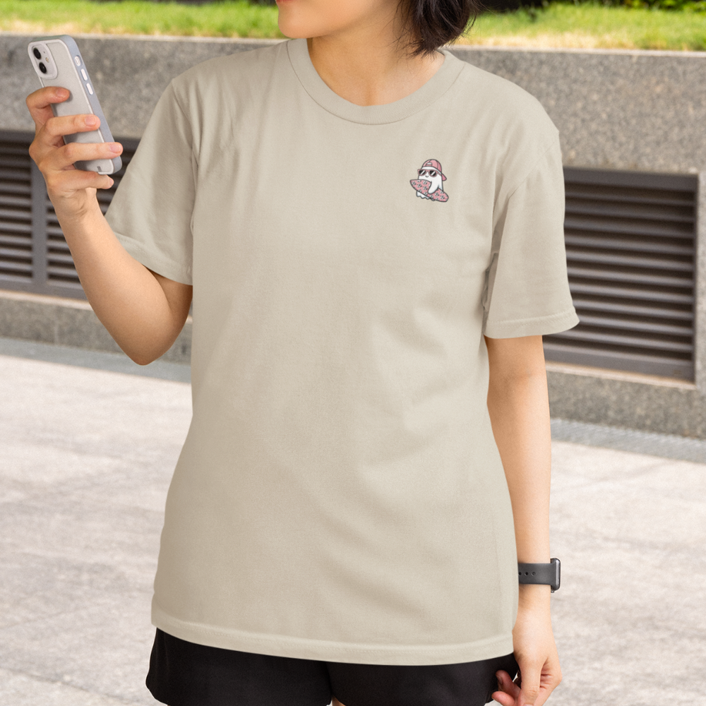 Person wearing a beige t-shirt with a small graphic on the chest, holding a phone.