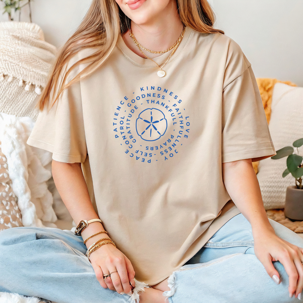 Person wearing a beige t-shirt with blue circular design and text, sitting on a couch.
