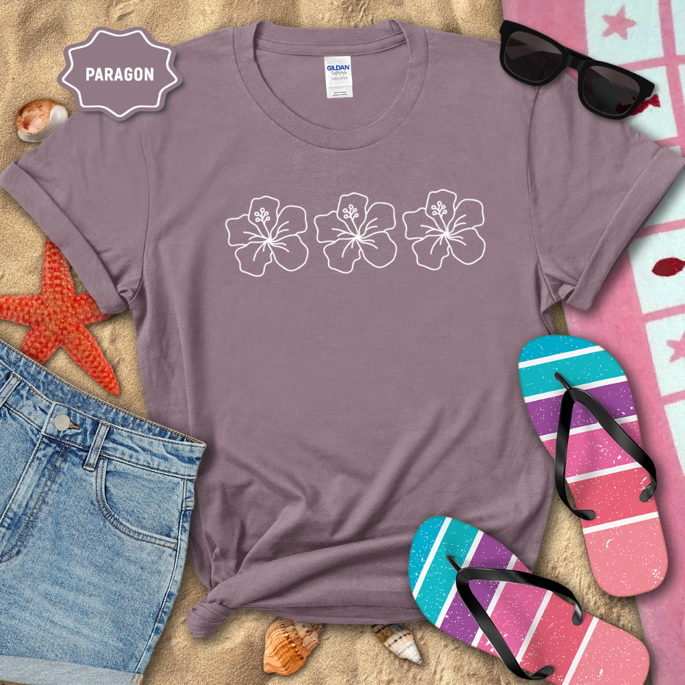 Purple t-shirt with floral designs on a sandy surface with beach accessories.
