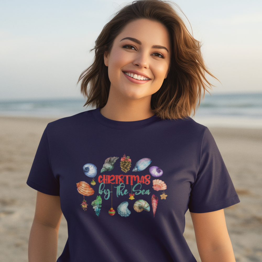 Woman wearing a navy blue t-shirt with 'Christmas by the Sea' design on a beach.