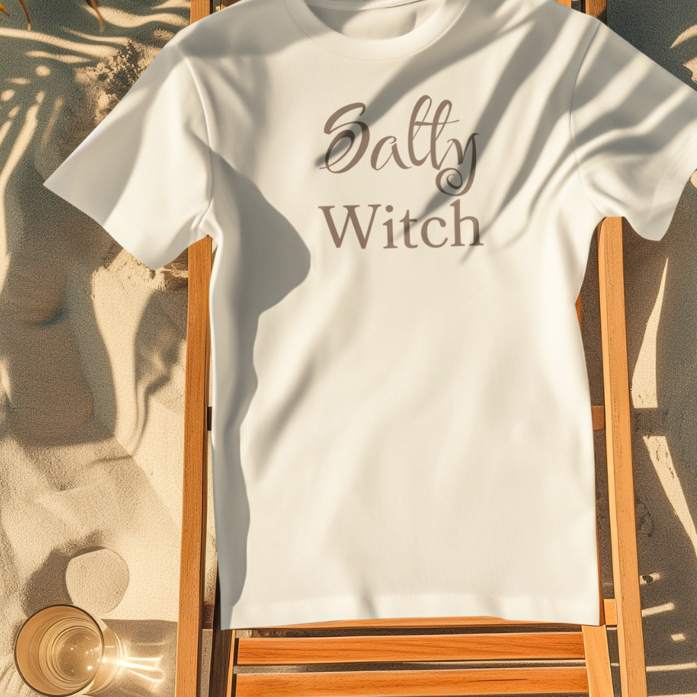 White t-shirt with 'Salty Witch' text on a wooden chair with sand and palm leaves in the background