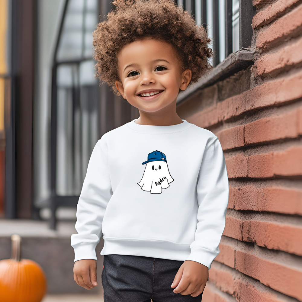 Child wearing a white sweatshirt with a ghost design, standing against a brick wall.