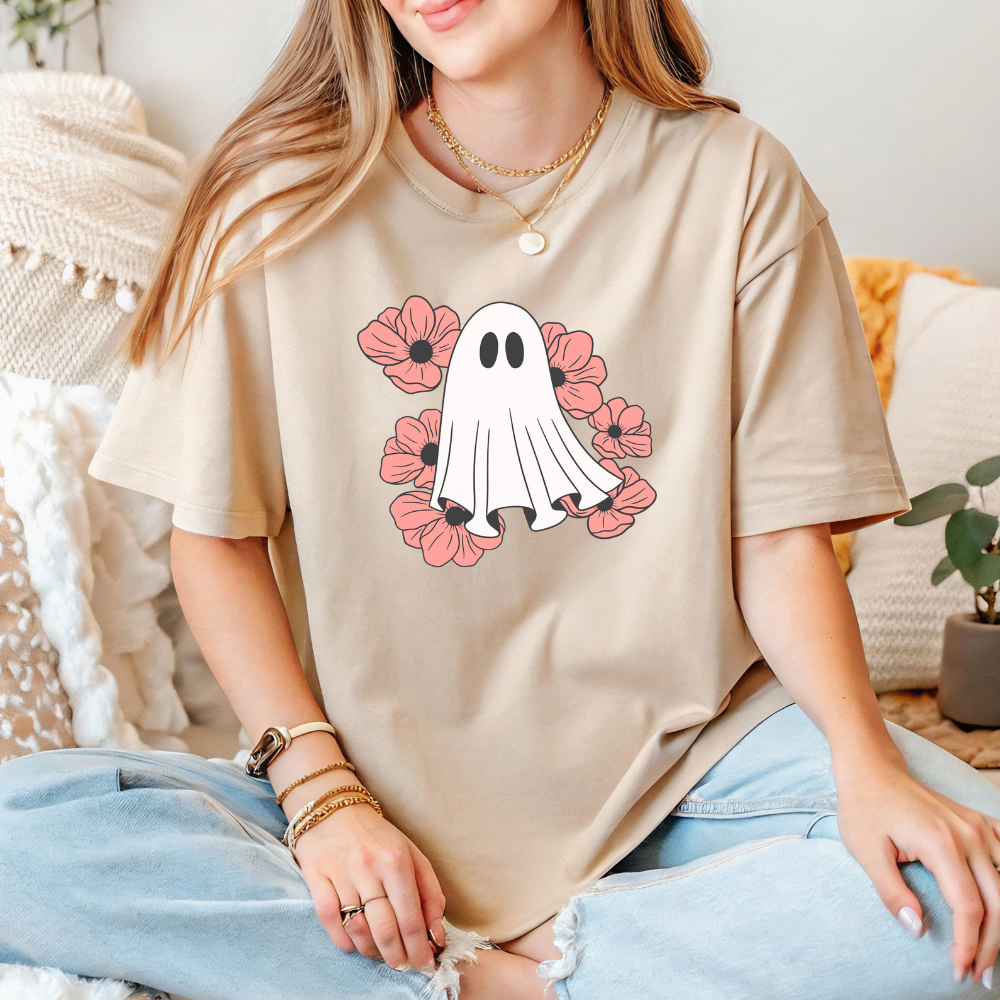 Person wearing a beige t-shirt with a ghost and flower design, sitting on a couch.