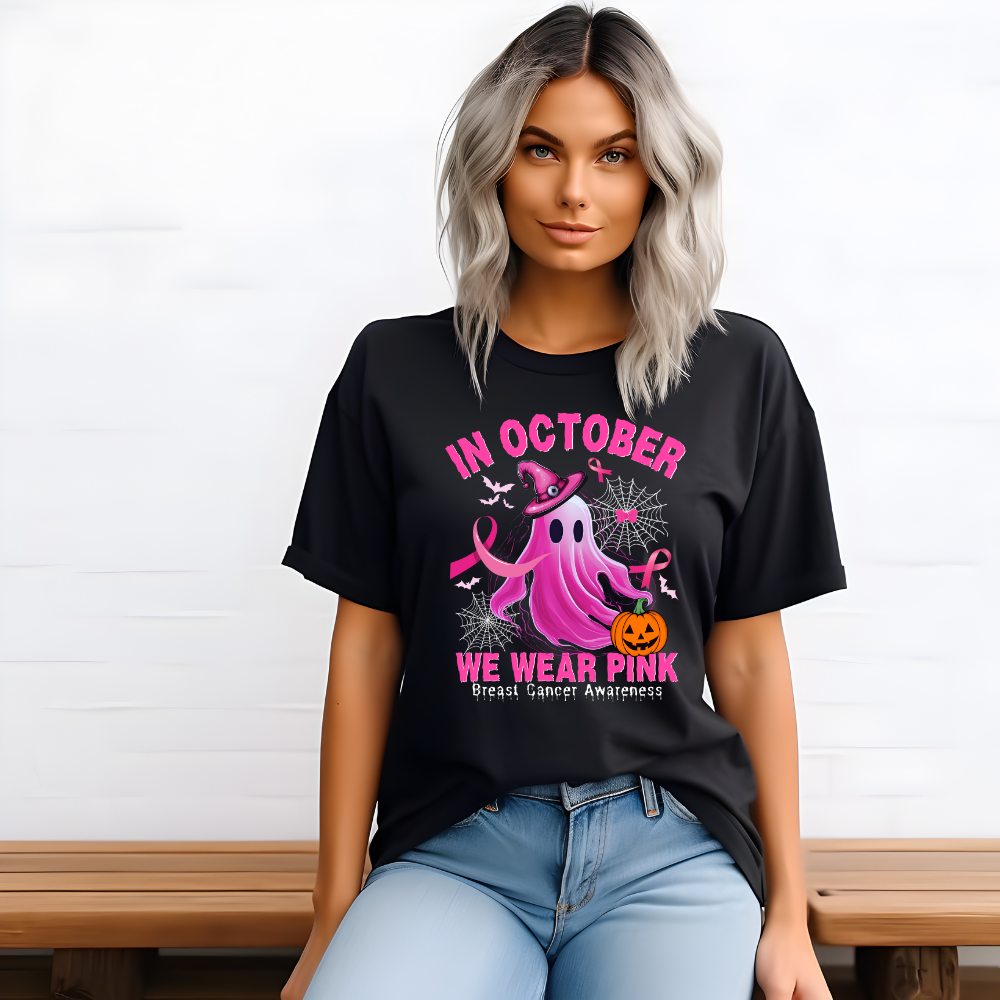 A woman wearing a black t-shirt with the text 'In October We Wear Pink' and a graphic of a pink ghost with a witch hat.