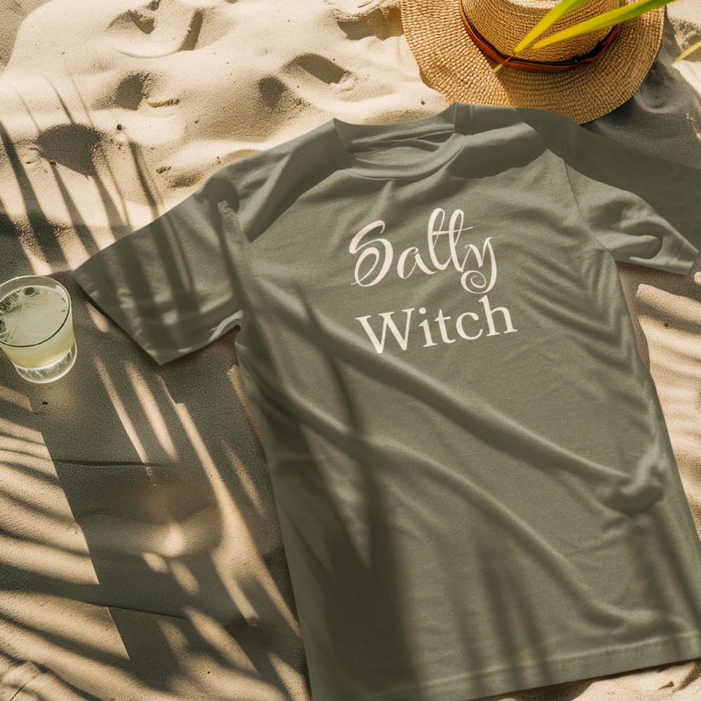 Green t-shirt with 'Salty Witch' text on a sandy surface with a hat and glass of lemonade.