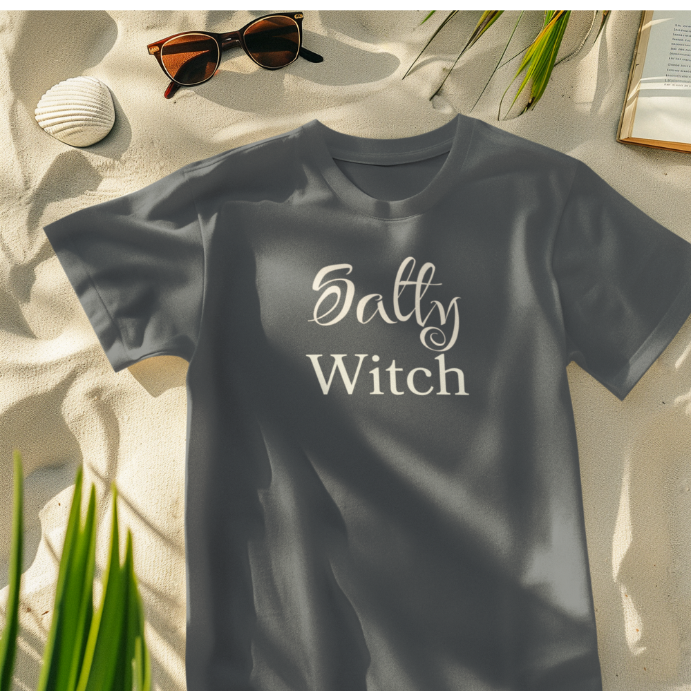 Gray t-shirt with 'Salty Witch' text on a sandy background with sunglasses and a book.