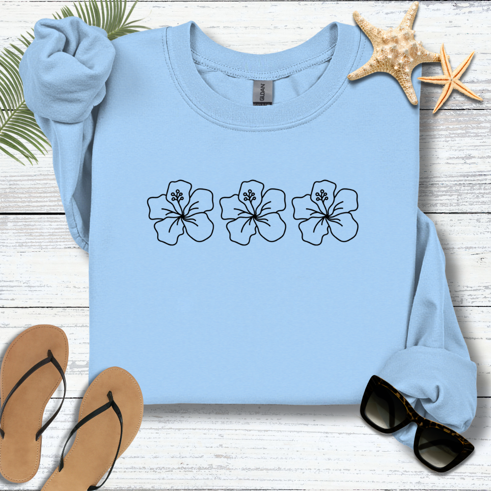 Light blue sweatshirt with floral designs on a wooden surface with flip-flops and sunglasses.