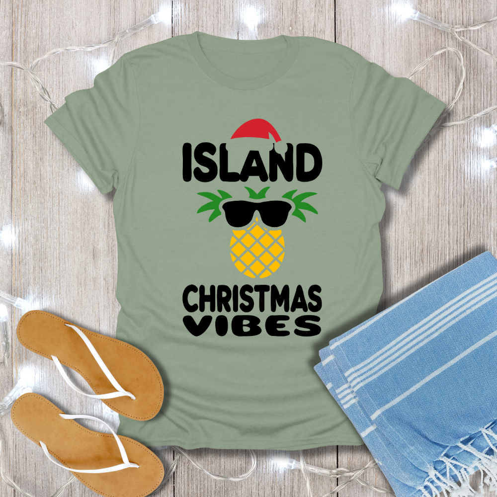 Green t-shirt with 'Island Christmas Vibes' design on a wooden surface with flip-flops and a towel.