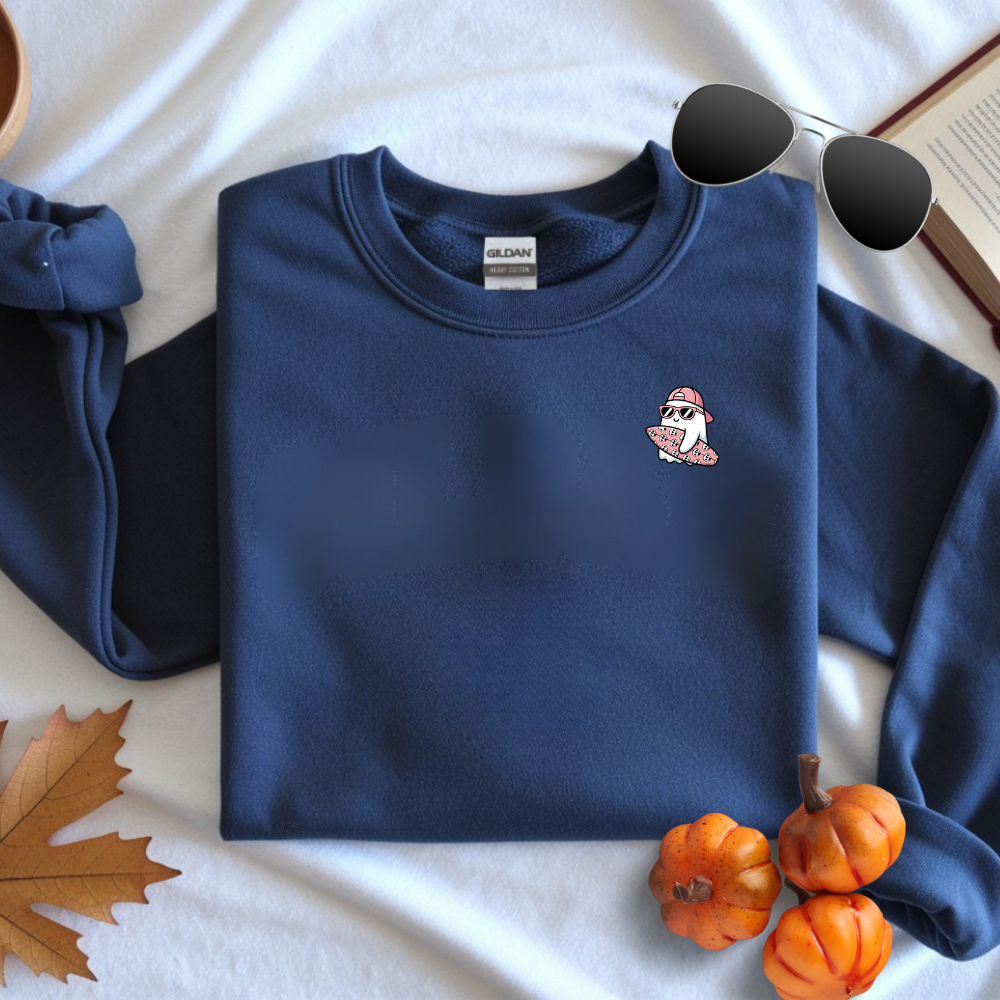 Folded navy blue sweatshirt with a small white penguin design on a light background with pumpkins and leaves.