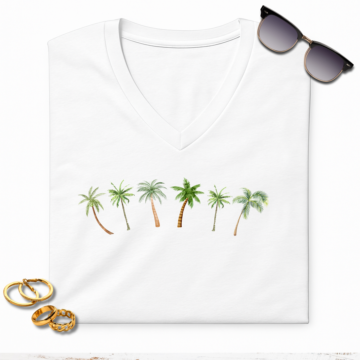 White t-shirt with palm tree design, sunglasses, and gold rings on a white background
