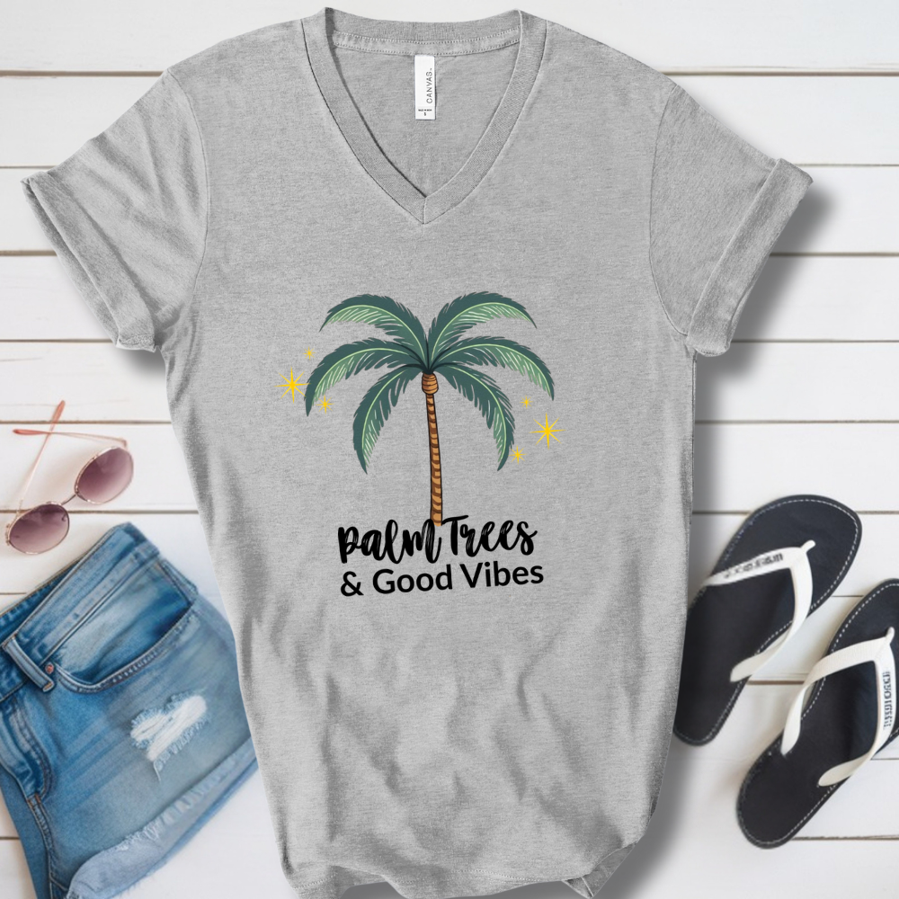Gray t-shirt with palm tree design and 'Palm Trees & Good Vibes' text on a wooden surface with sunglasses and shorts.