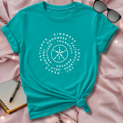 Turquoise t-shirt with motivational text and design on a pink surface with sunglasses and notebook.