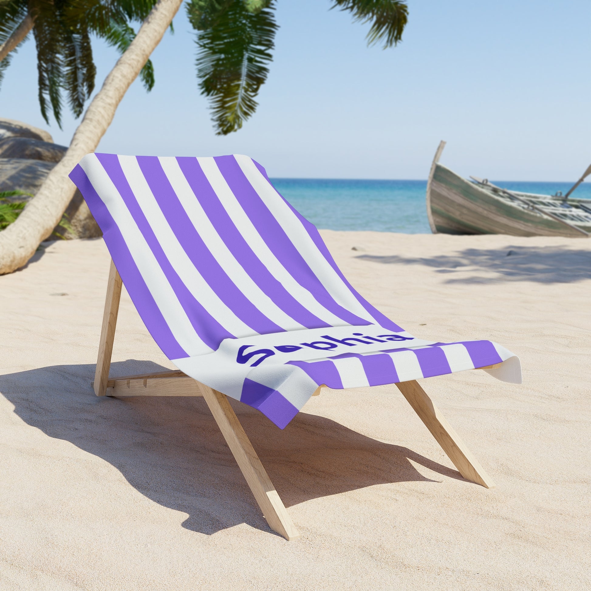 Beach chair with a purple and white striped towel on a sandy beach with palm trees and ocean in the background.