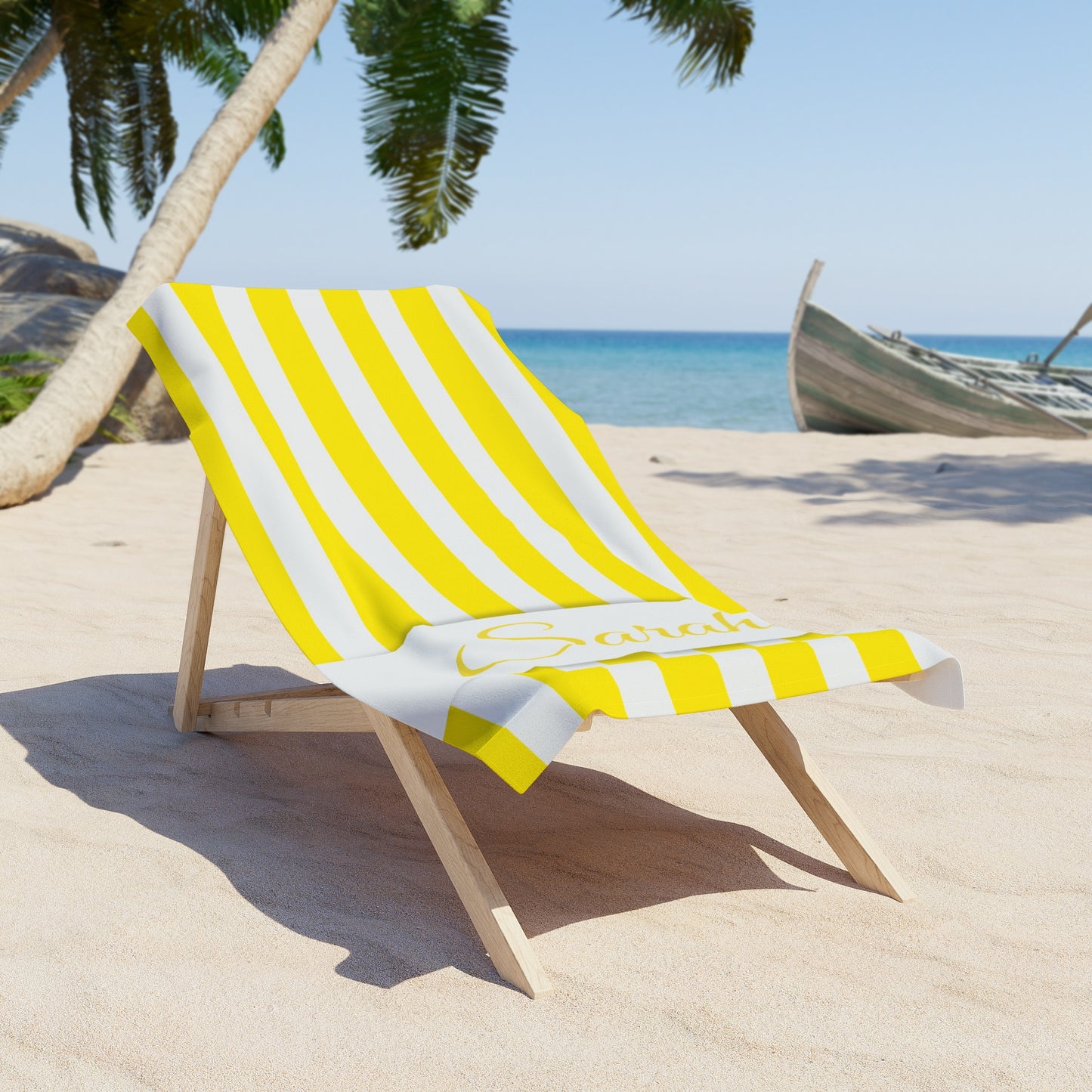 Yellow and white striped beach towel on a wooden chair at a sandy beach with palm trees and ocean in the background.
