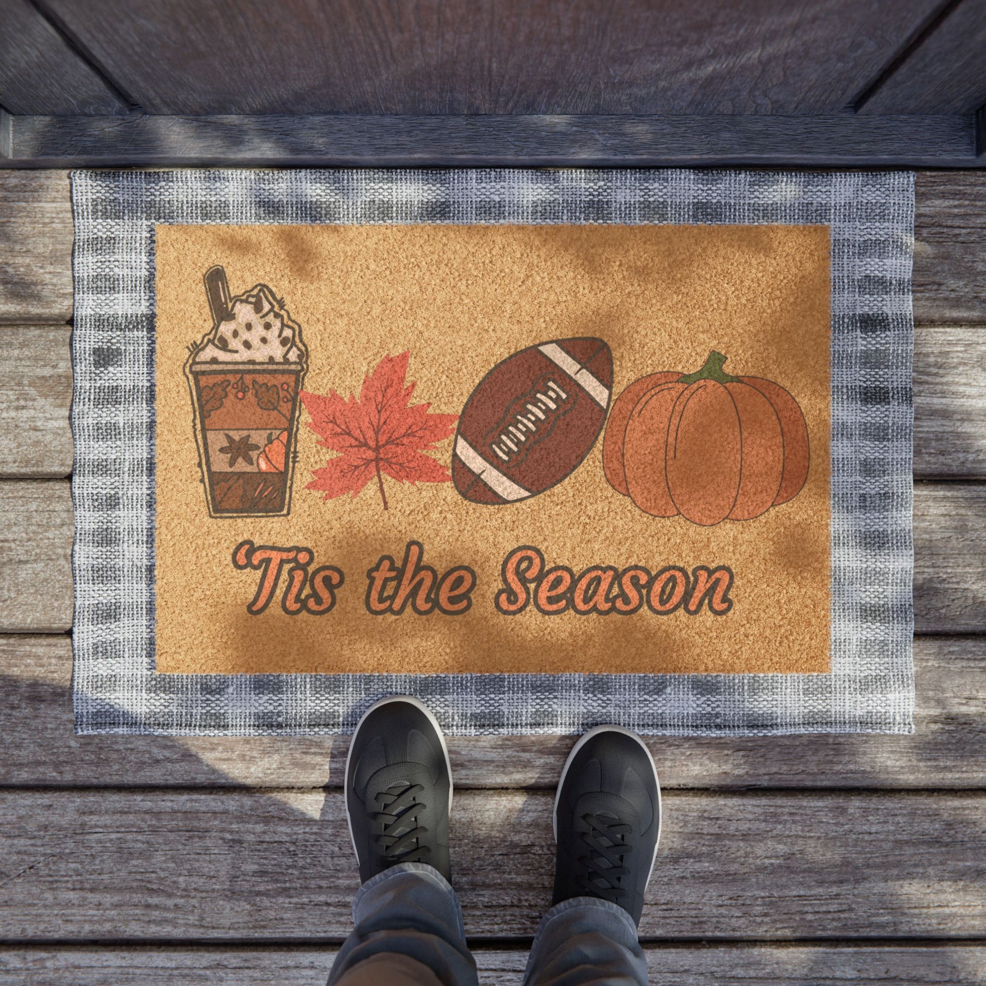 Doormat with autumn-themed design featuring a coffee cup, leaf, football, and pumpkin on a wooden floor.