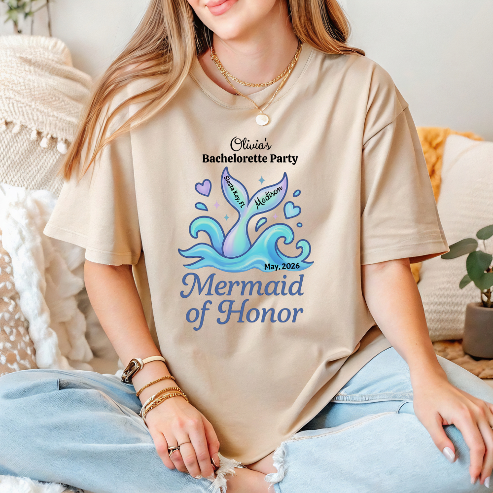Person wearing a beige t-shirt with a mermaid-themed design and text.