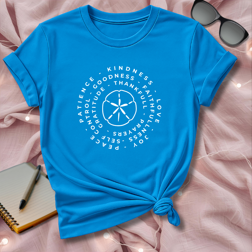 Blue t-shirt with white text and design on a pink surface with sunglasses and notebook.