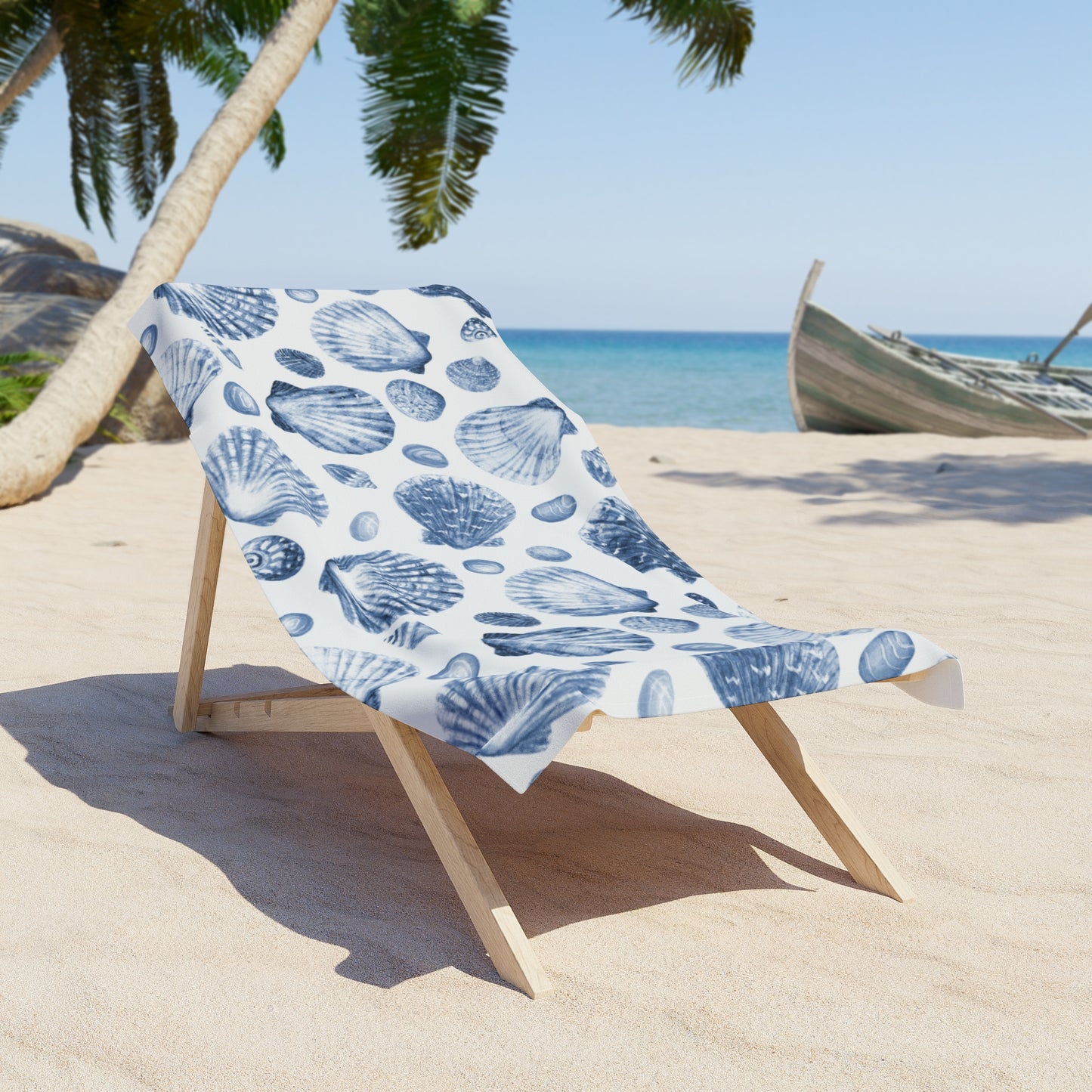 Beach chair with a blue shell patterned towel on a sandy beach with palm trees and ocean in the background.