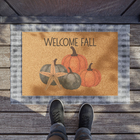 Doormat with 'Welcome Fall' text and pumpkins on a wooden floor.