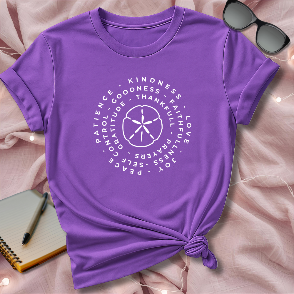 Purple t-shirt with white text and design on a pink surface with sunglasses and notebook.