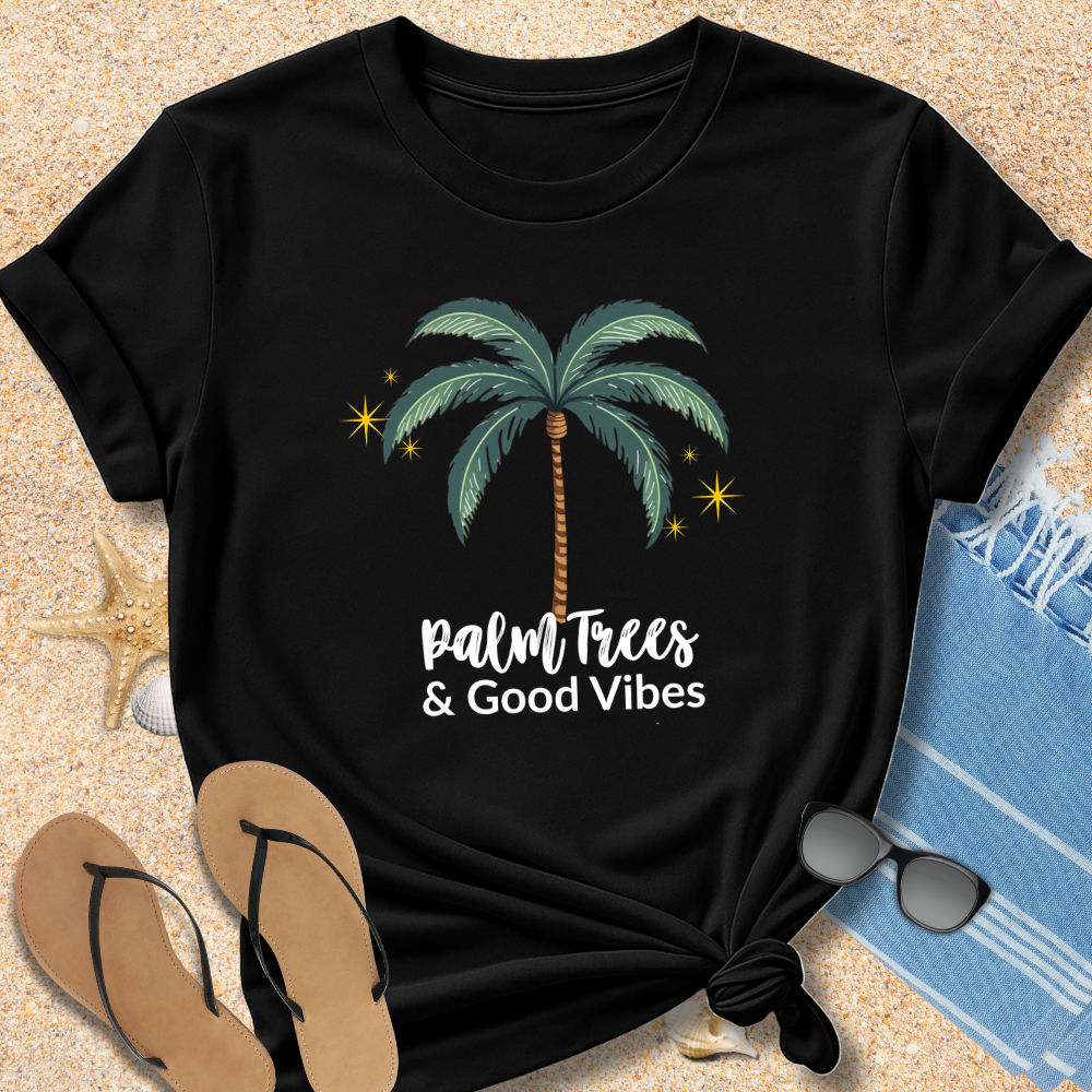 Black t-shirt with palm tree design and 'Palm Trees & Good Vibes' text on sand with flip-flops and towel.