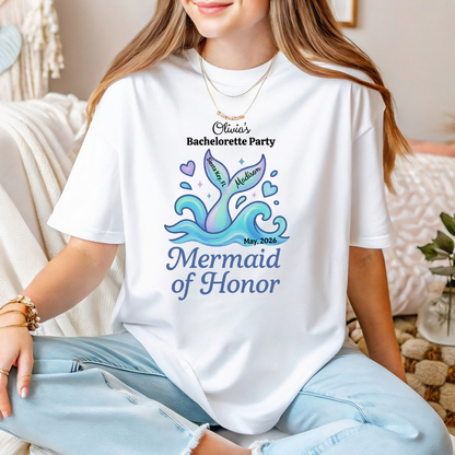 Person wearing a white t-shirt with a mermaid-themed design and text, sitting on a couch.