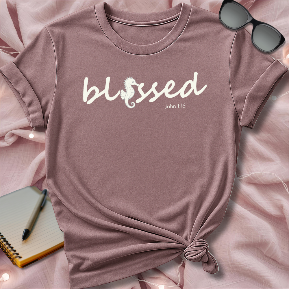 Pink t-shirt with 'blessed' text on a pink surface with sunglasses and notebook.