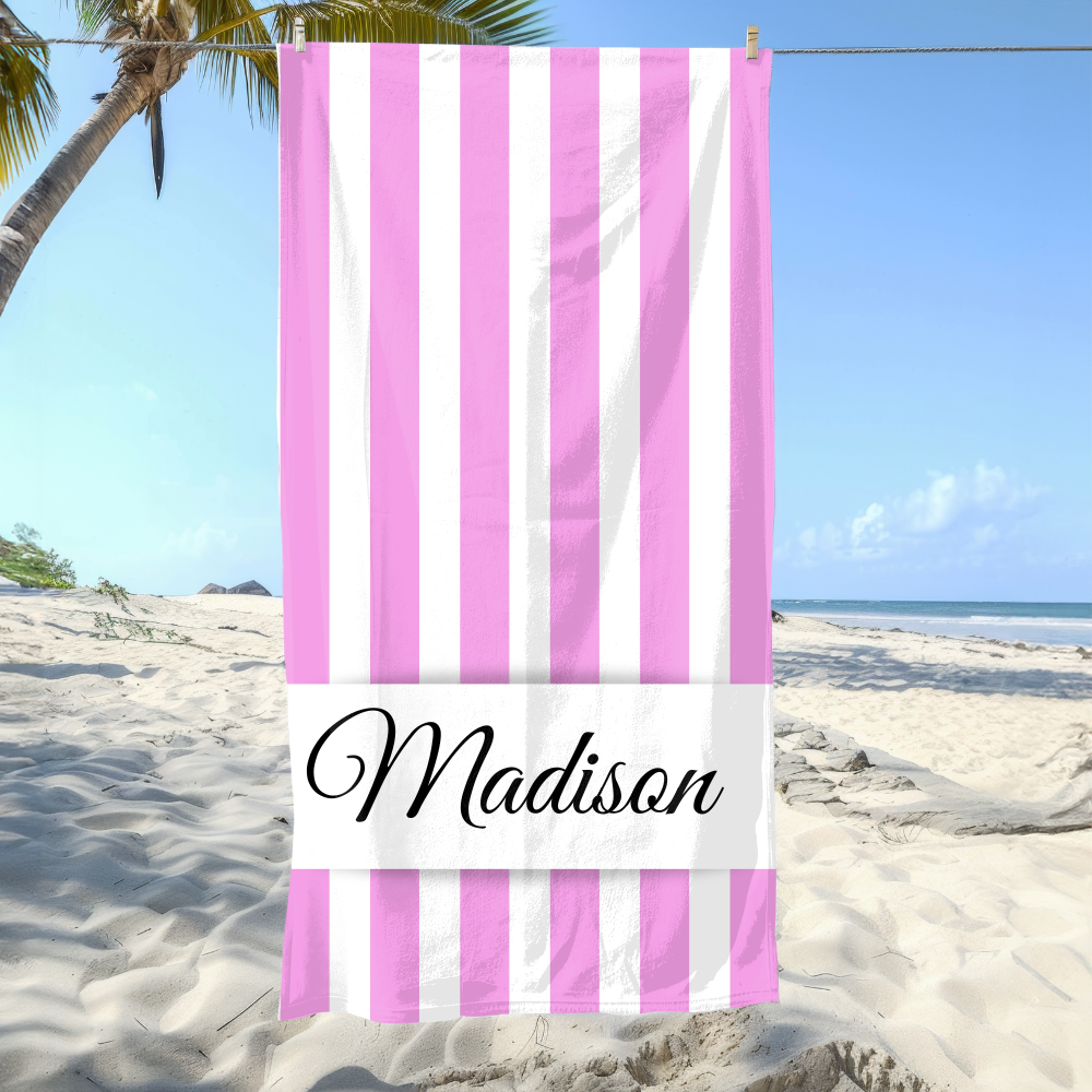 Striped beach towel with 'Madison' branding on a sandy beach with palm trees and blue sky.