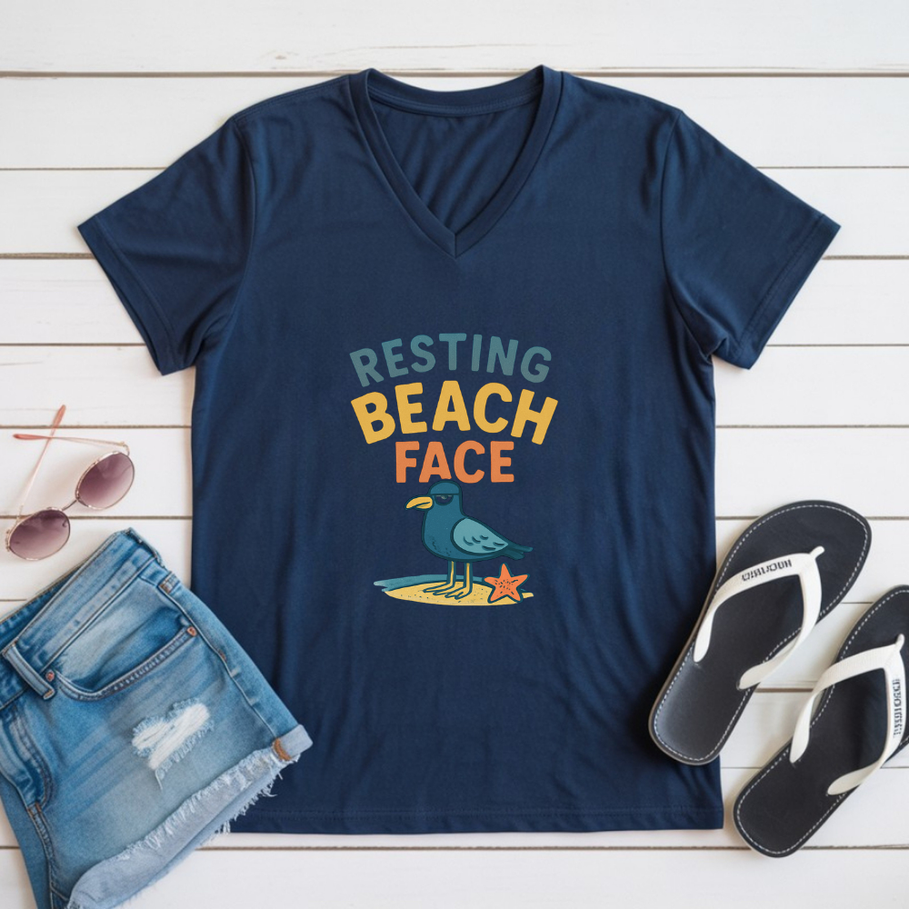 Navy blue t-shirt with 'Resting Beach Face' graphic on a wooden surface with sunglasses and sandals.