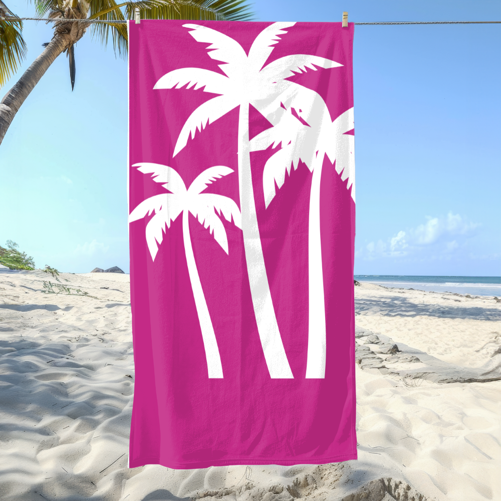 Pink beach towel with white palm tree design hanging on a clothesline over a sandy beach.