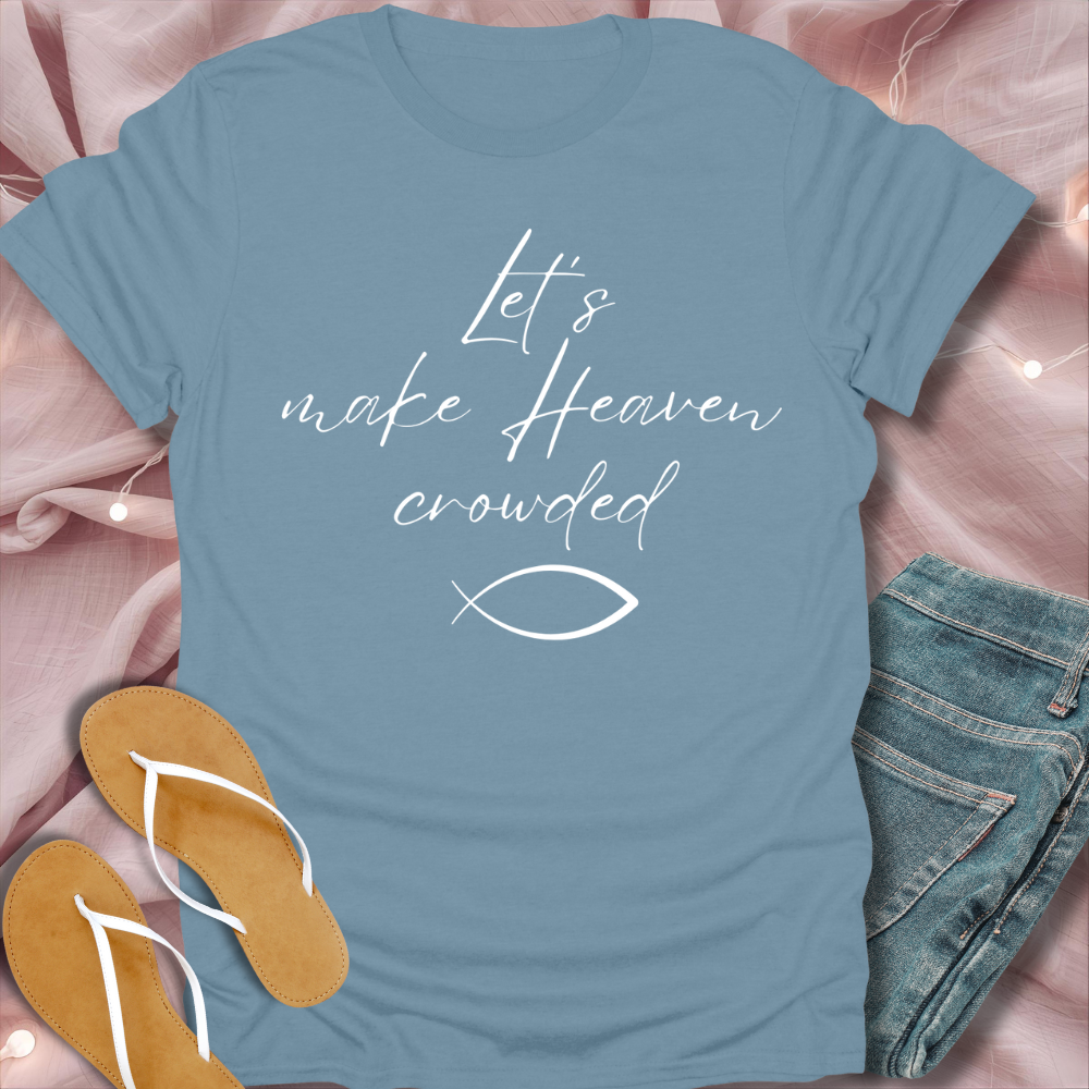 Blue t-shirt with 'Let's make Heaven crowded' text and fish symbol on a pink fabric background.