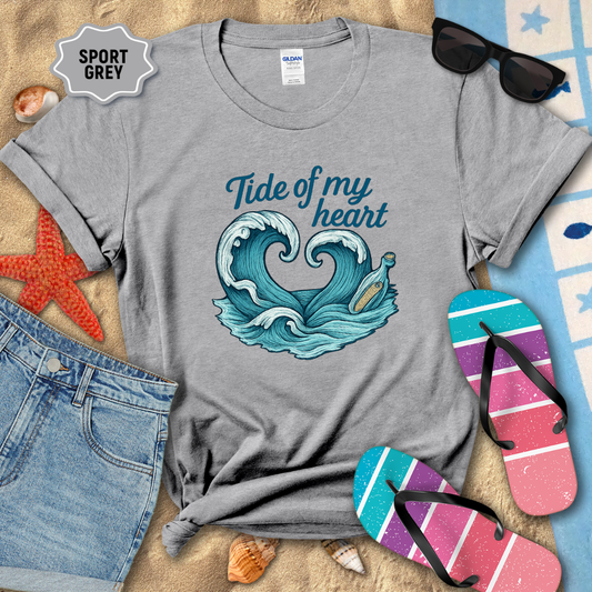 Gray t-shirt with wave design and text 'Tide of my heart' on a beach-themed background with sunglasses, flip-flops, and starfish.
