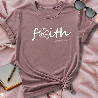 Pink t-shirt with 'faith' text on a pink surface with sunglasses and notebook.