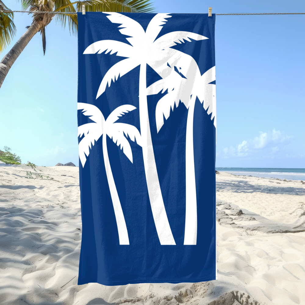 Beach towel with white palm tree design on a blue background, hanging on a beach.