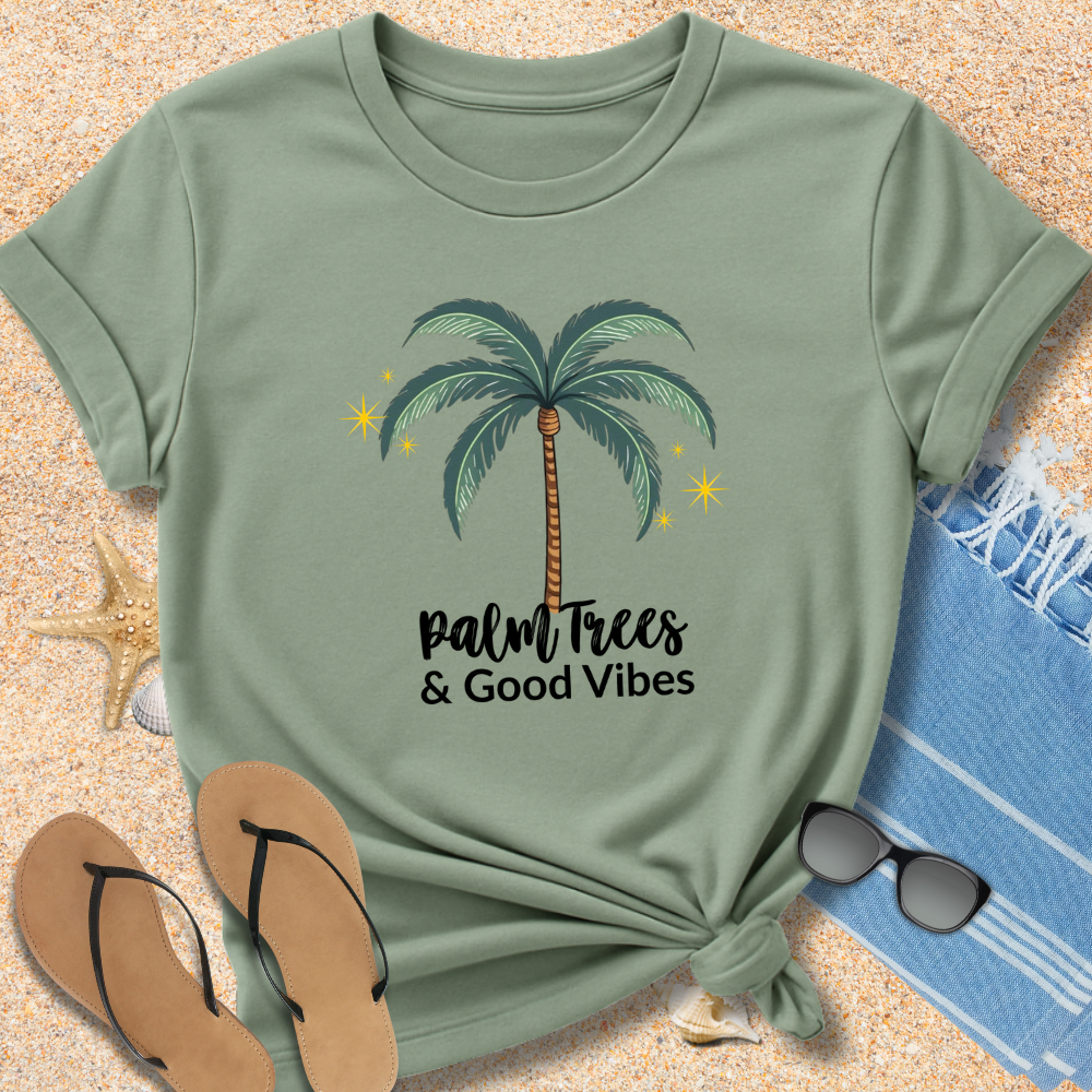 Green t-shirt with palm tree design and 'Palm Trees & Good Vibes' text on sand with beach accessories.