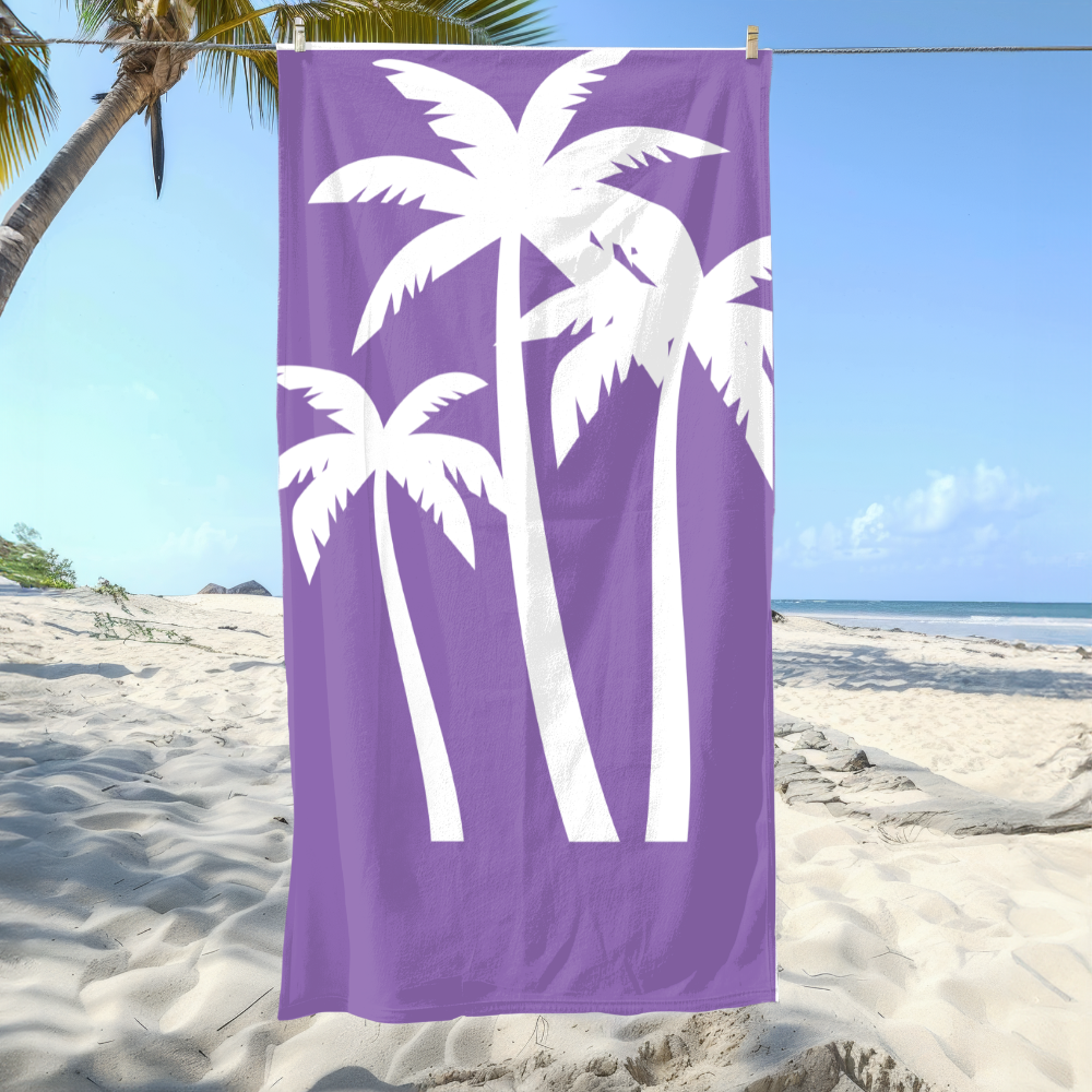 Purple beach towel with white palm tree design hanging on a clothesline over a sandy beach.