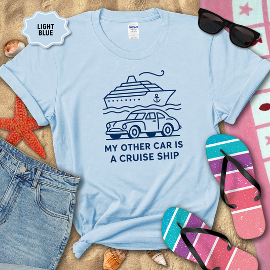 Light blue t-shirt with a cruise ship graphic and text on a sandy background with beach accessories.