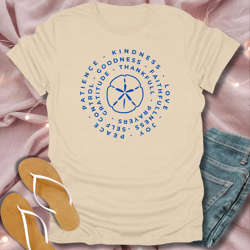 Beige t-shirt with blue circular design and text on a pink surface with jeans and sandals.