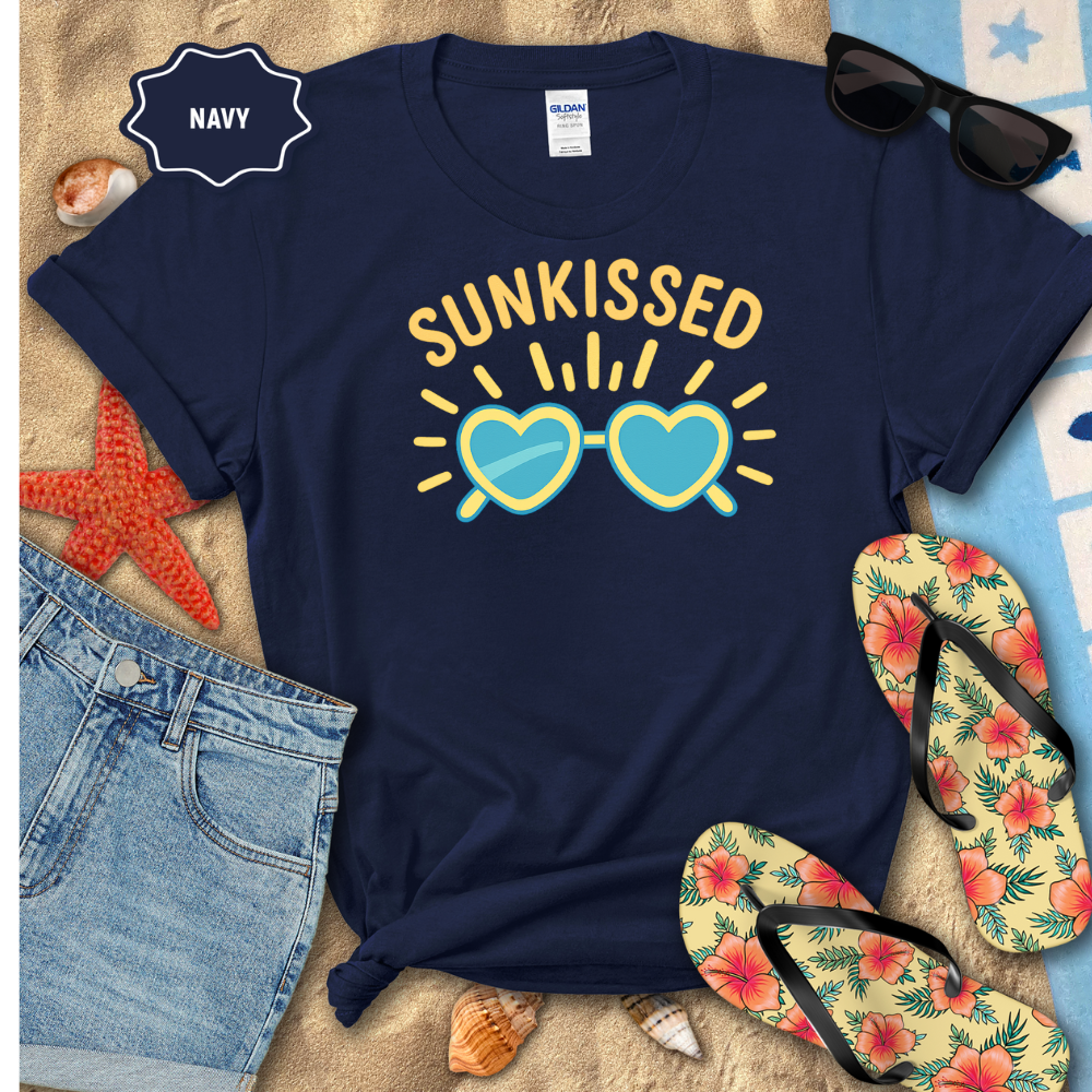 Navy t-shirt with 'Sunkissed' design on a beach-themed background with sunglasses, flip-flops, and denim shorts.