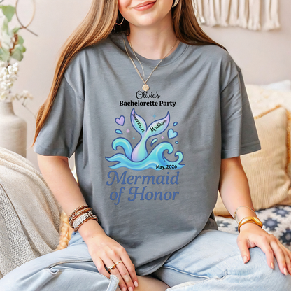 Person wearing a gray t-shirt with a mermaid design and text, sitting on a couch.
