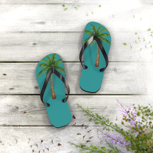 Pair of blue flip-flops with palm tree design on a wooden surface with flowers.