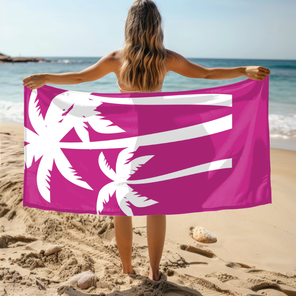 Person holding a pink towel with white palm tree designs on a beach.