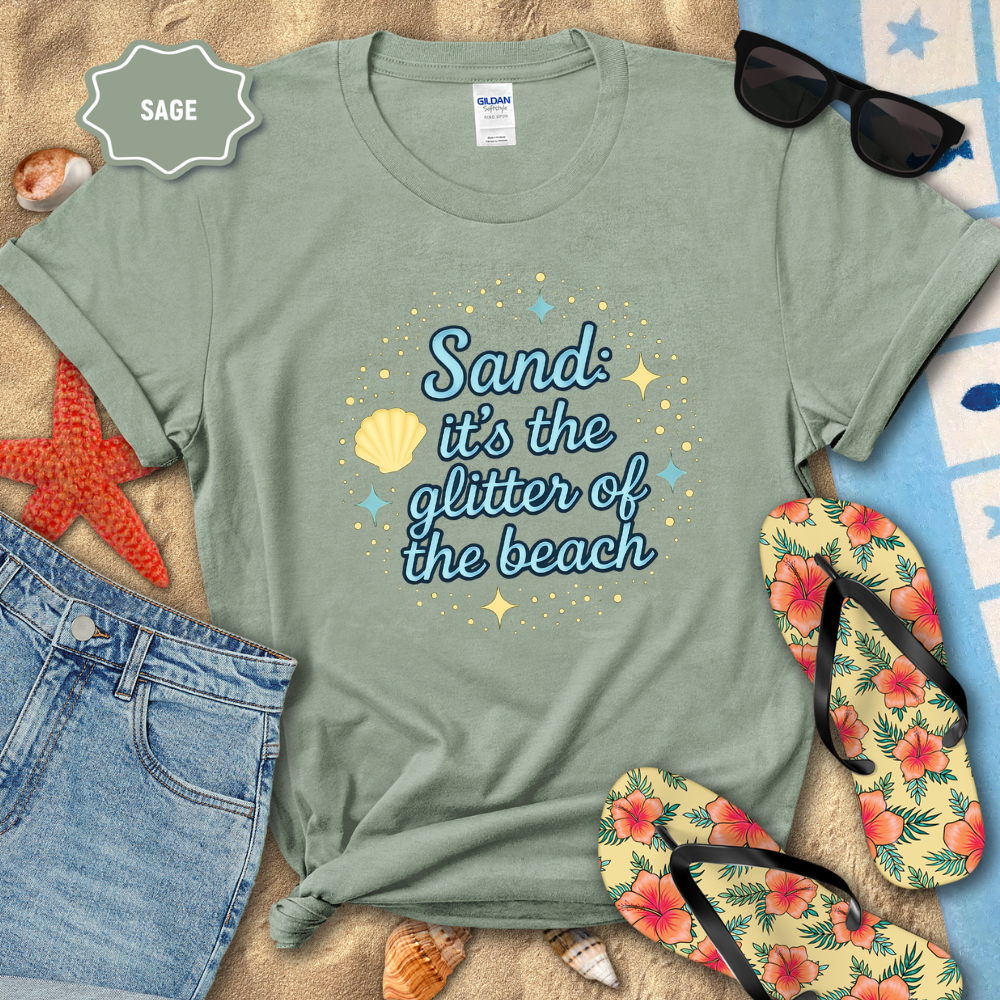 Sage green t-shirt with beach-themed text on a sandy background with flip-flops and sunglasses.